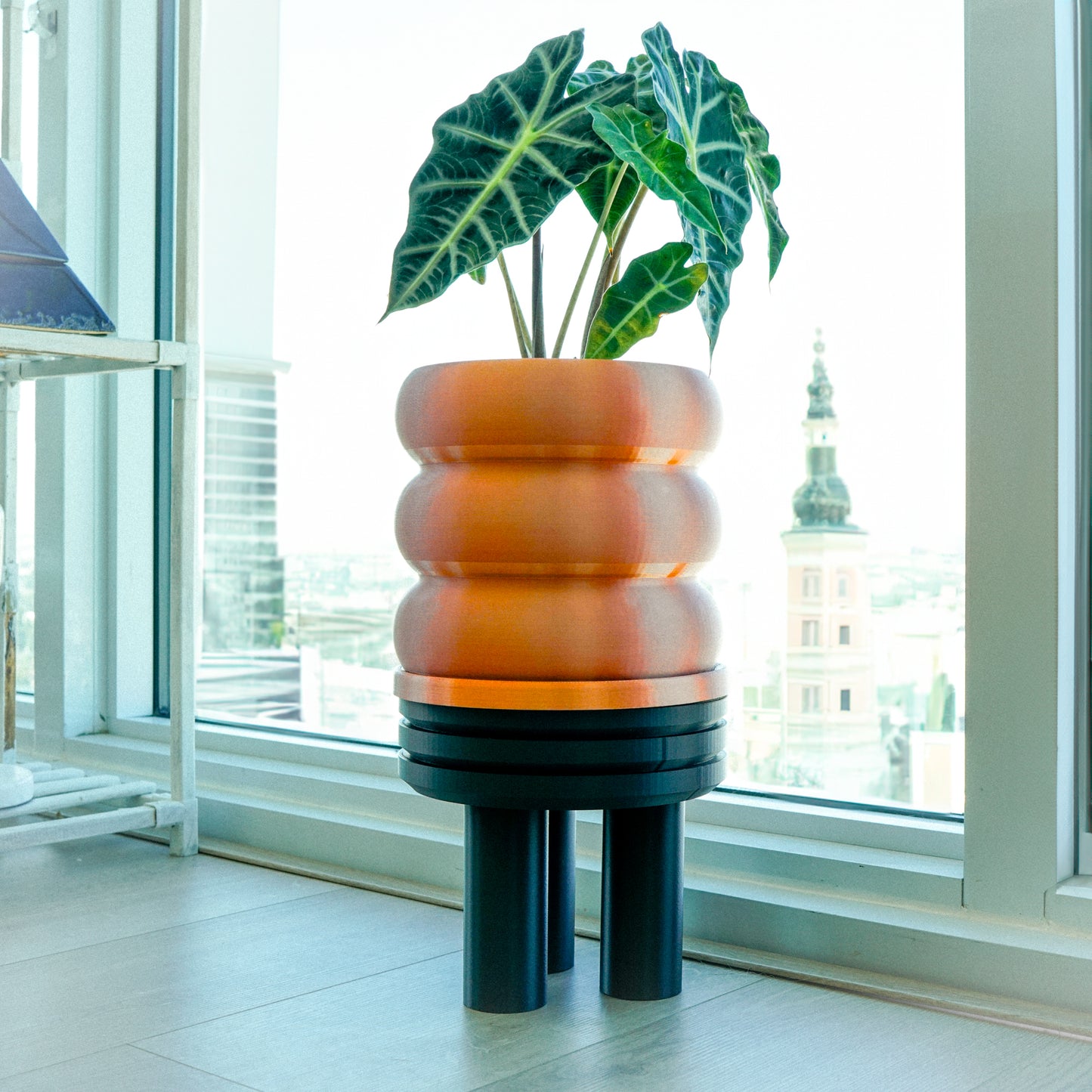 Bubble Planter with Drainage, resembling a stack of donuts, in a sleek metallic finish, elegantly displaying greenery against a modern, cityscape background; perfect for plant lovers and home decor enthusiasts seeking excellent drainage and multiple color options.