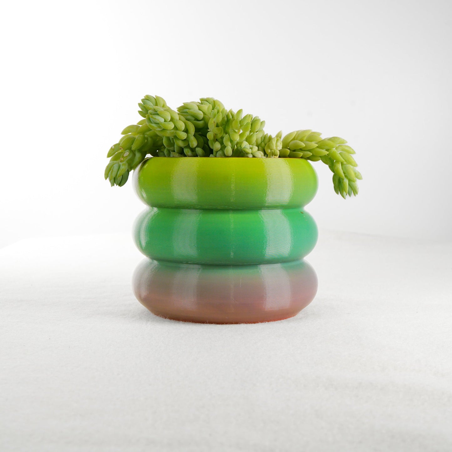 Bubble Planter resembling a stack of donuts, showcasing a gradient of green and brown hues, with succulent plants. Perfect for plant lovers, this home decor piece offers excellent drainage and multiple color options.