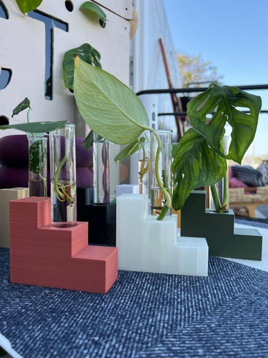 A collection of Step Stand Propagation Stations in multiple colors, made from eco-friendly materials, showcasing their excellent drainage and modern design, ideal for plant lovers and home decor enthusiasts. The stands feature glass tubes holding green plant cuttings, making them a captivating and perfect housewarming gift or wedding centerpiece.